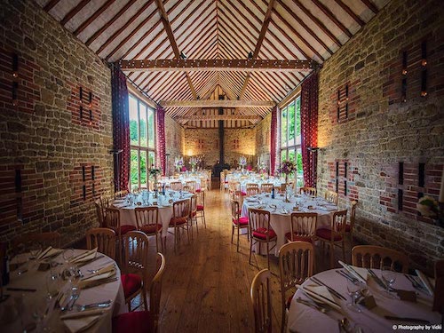 Inside Bartholomew Barn with tables set up for a wedding reception, very large round floral arrangement hanging from ceiling