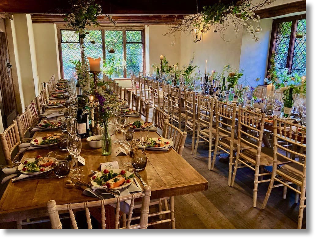 The dining room at Pilgrims Rest in Battle, East Sussex, tables are set up with glassware, npakins, floral arrangements and a plated smoked salmon terrine starter course