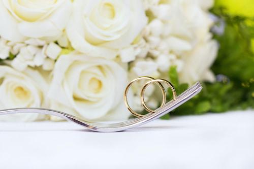 Wedding rings on a fork with a bunch white roses in the background.