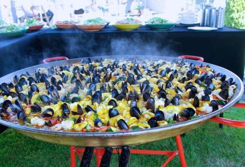 Large steaming pan of seafood paella with salads in the background.