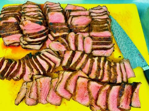 Sliced strip sirloin of beef on a yellow chopping board with a Damascus knife.
