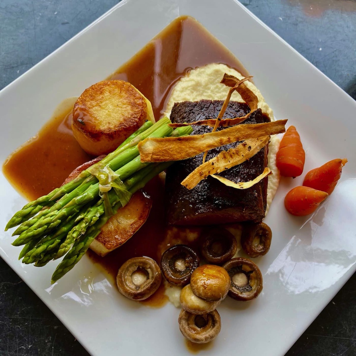 Plated venison loin with fondant potatoes, asparagus, mushrooms, carrots with veal reduction