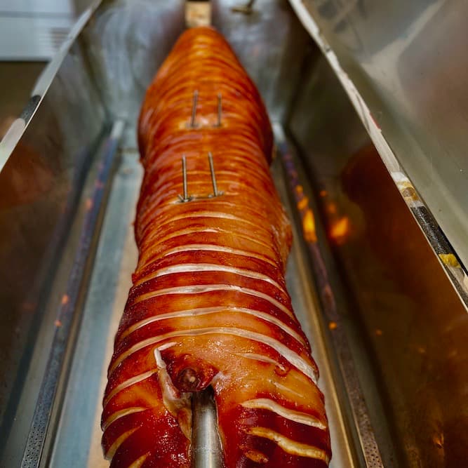 Whole pig being cooked in the hog roast machine showing the burners with flames