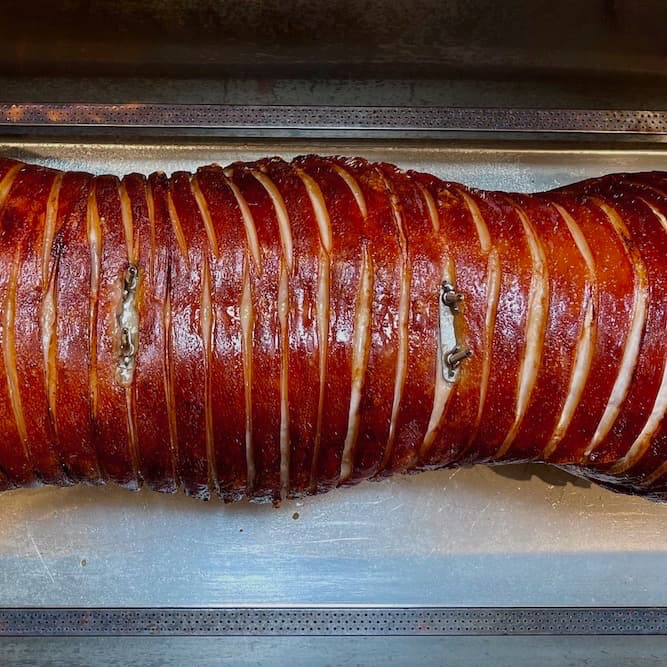 Hog roast with golden dark crackling next to gas burners inside hog roast machine